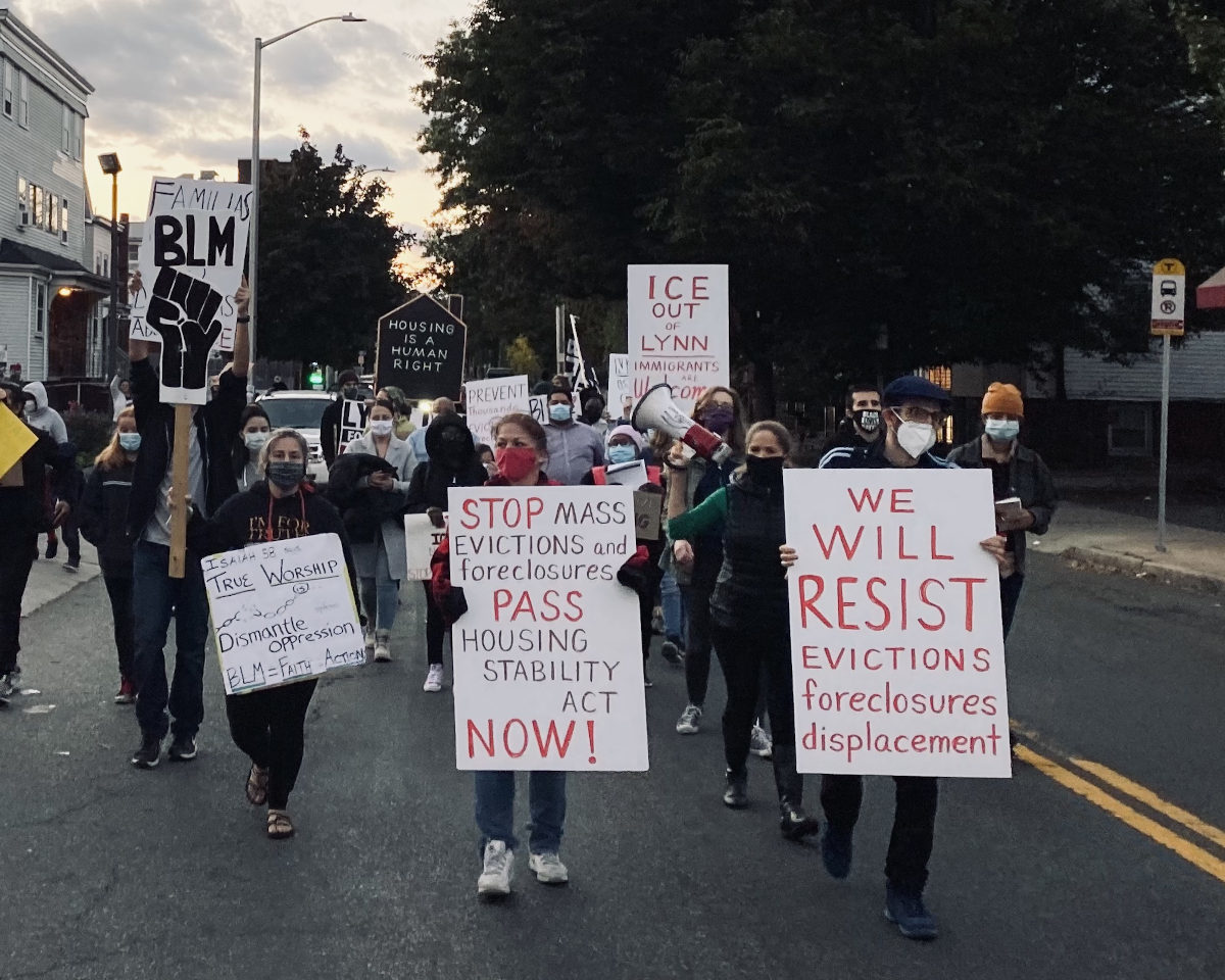 photo of protest march in the street with signs referencing housing justice and immigrant rights